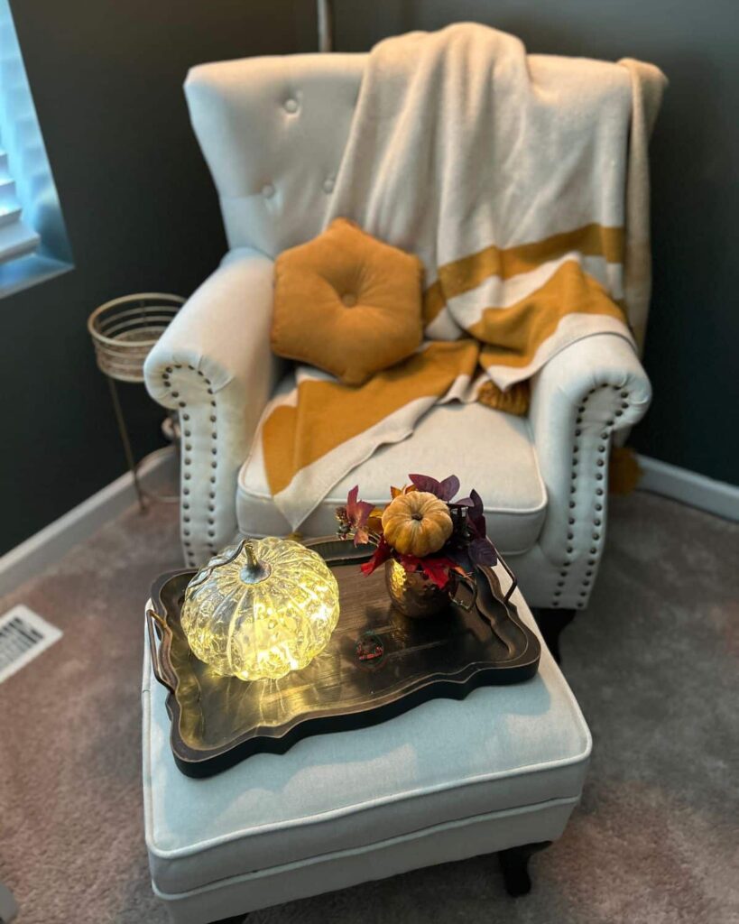 A cozy autumn chair with an orange and white blanket and light colored orange pillow on it.