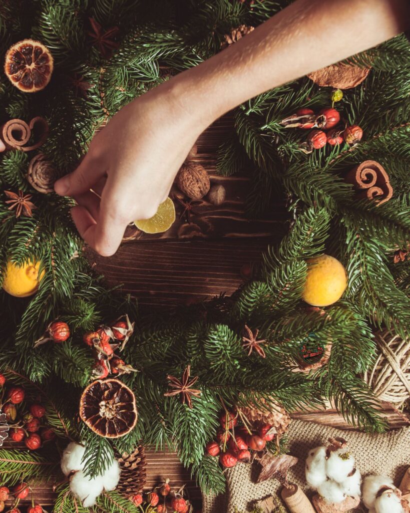 A hand that is decorating a pine wreath with dried orange slices.