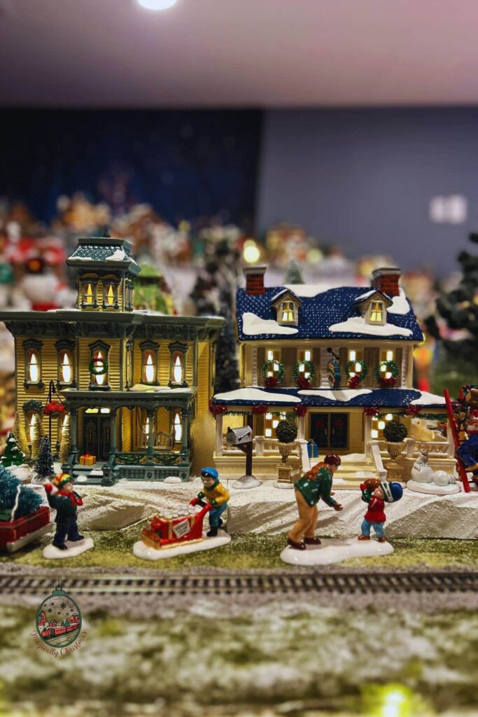 Two Christmas village house with some people outside of it.